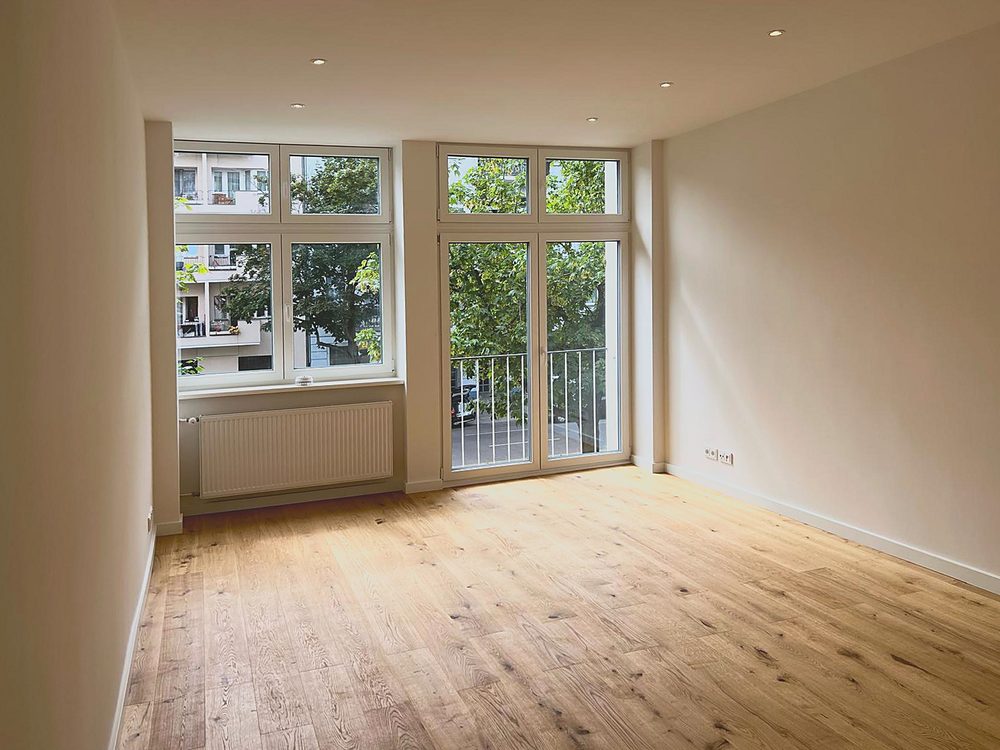 Wohnraum der Mitarbeiterwohnung mit Balkontür und Eichenparkett